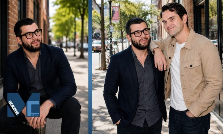 Colin Carr wearing a navy blazer and thick glasses alongside his comedian brother Jimmy Carr on a city street.