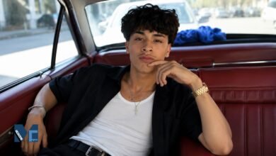 Alex Chino, known as @youcantfindalex, posing inside a vintage car wearing a black shirt and white tank top in a lifestyle portrait.