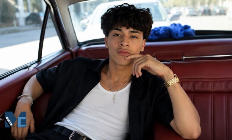 Alex Chino, known as @youcantfindalex, posing inside a vintage car wearing a black shirt and white tank top in a lifestyle portrait.
