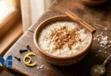 A traditional clay bowl filled with creamy arroz con leche boliviano, heavily dusted with ground cinnamon, placed on a wooden table alongside cinnamon sticks and cloves.