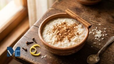 A traditional clay bowl filled with creamy arroz con leche boliviano, heavily dusted with ground cinnamon, placed on a wooden table alongside cinnamon sticks and cloves.