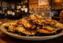 A premium close-up shot of crispy golden berenjenas con miel drizzled with dark sugarcane molasses on a rustic plate, perfect for finding the best Andalusian tapas near you.