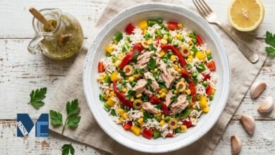 A colorful bowl of authentic Spanish ensalada de arroz featuring fluffy white rice, tuna, green olives, corn, peas, and roasted red peppers on a rustic table.