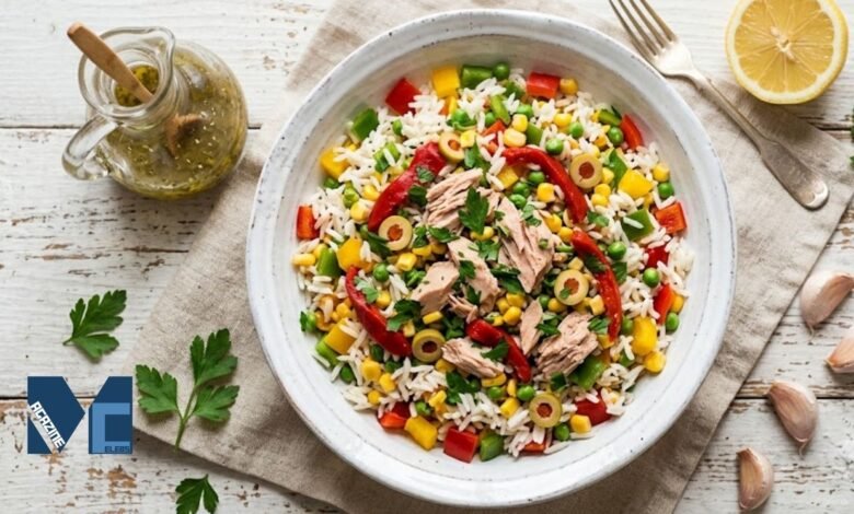 A colorful bowl of authentic Spanish ensalada de arroz featuring fluffy white rice, tuna, green olives, corn, peas, and roasted red peppers on a rustic table.