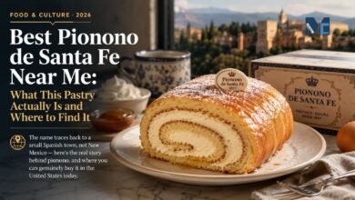 A traditional Pionono de Santa Fe rolled sponge cake filled with cream and topped with toasted sugar, served on a plate with a vintage bakery box and the city of Granada in the background.