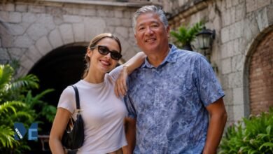 A warm portrait of Chris Rodrigo smiling alongside his daughter, global pop star Olivia Rodrigo, standing together in a scenic outdoor setting with stone archways.