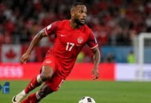 Cyle Larin in action for Canada during an international football match, sprinting with the ball on the pitch.