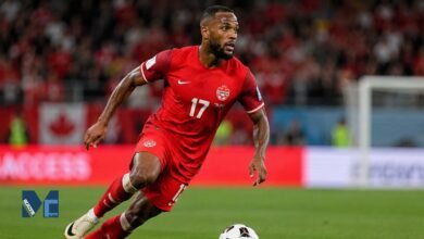 Cyle Larin in action for Canada during an international football match, sprinting with the ball on the pitch.