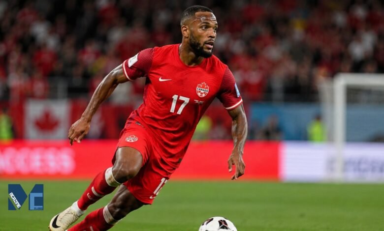 Cyle Larin in action for Canada during an international football match, sprinting with the ball on the pitch.