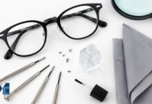 Eyeglass repair kit showing precision screwdrivers, spare screws, nail varnish, microfibre cloth, and glasses on a white surface for fixing loose eyeglasses at home.