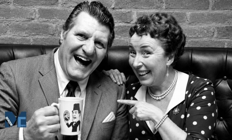 A black and white vintage photograph of British comedian Tommy Cooper laughing with a mug in his hand, while his wife Gwen Cooper smiles and playfully points at the mug.