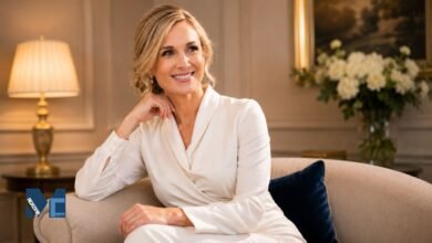 A premium portrait of Harriet Sperling sitting gracefully on a sofa, wearing an elegant ivory wrap-style dress in a classic, warmly lit room.