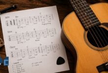 Printed guitar tablature sheet with handwritten notes beside an acoustic guitar on a wooden surface