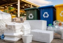 White Styrofoam food containers and foam packaging placed beside recycling bins at a modern recycling facility in the United States.