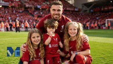 Former Liverpool captain Jordan Henderson smiling on the Anfield pitch surrounded by his three children, including his eldest daughter Elexa Henderson, all wearing Liverpool kits.