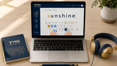 A laptop screen displaying the Touch-Type Read and Spell (TTRS) online platform interface with visual keyboard guides, alongside a TTRS notebook and headphones on a wooden desk.